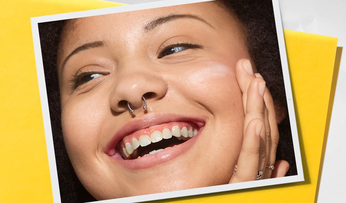 Smiling model with a septum piercing and a hand on their face